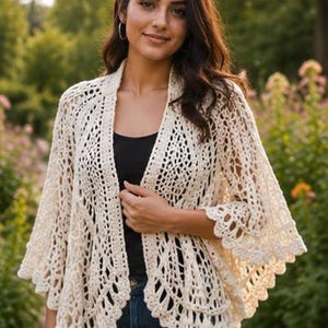May include: An off-white, open-front crochet cardigan featuring an intricate, airy lace pattern with a scalloped edge along the hem and wide, flared sleeves. The garment is worn over a simple black top and blue denim jeans, showcasing a delicate texture.