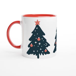 Könnte beinhalten: Weißer Keramikbecher mit roter Innenseite und Henkel. Der Becher zeigt ein marineblaues Weihnachtsbaumdesign mit roten Kugeln und einem Stern oben. Eine festliche Urlaubstasse.