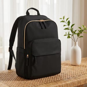 Peut inclure: Un sac à dos noir doté d'un grand compartiment principal et d'une poche avant plus petite, tous deux sécurisés par des fermetures éclair dorées. Le sac comprend des bretelles réglables, une poignée supérieure et des poches latérales.