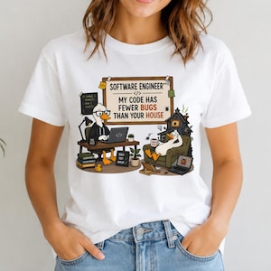 May include: A white t-shirt featuring a graphic of two ducks. One duck sits at a desk with a laptop and coffee, while the other relaxes in a chair. The text reads: SOFTWARE ENGINEER, MY CODE HAS FEWER BUGS THAN YOUR HOUSE, BUILD TEST DEPLOY, and ERROR 404.