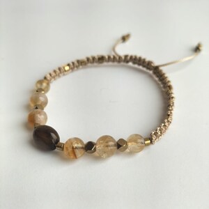May include: Beaded bracelet with amber and brown gemstones. The macrame cord has adjustable sliding knots. The beads are various shapes and sizes, with gold-coloured metal accents. The bracelet is suitable for a wrist size of approximately 15-20 cm.