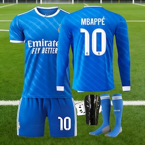 Könnte beinhalten: Ein blaues Fußball-Set mit einem Trikot mit kurzen und langen Ärmeln, Shorts, Socken und Schienbeinschonern. Die Trikots zeigen "Emirate FLY BETTER" und "MBAPPÉ 10". Shorts und Trikots haben weiße Akzente.