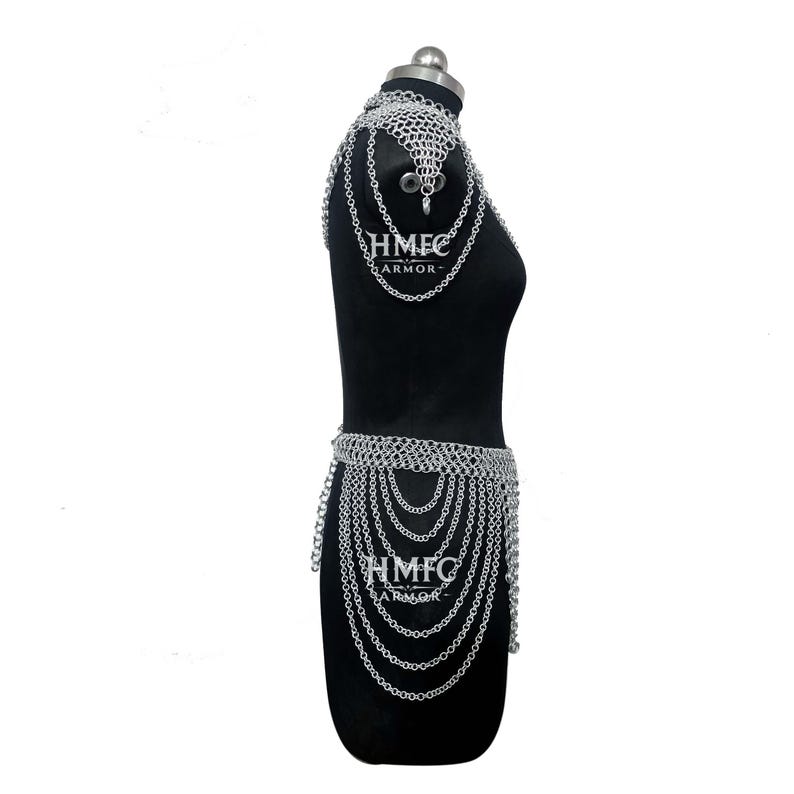 K&ouml;nnte beinhalten: Ein silberfarbenes Kettenhemd-Accessoire f&uuml;r Schulter und Taille mit ineinandergreifenden Metallringen. Das St&uuml;ck umfasst einen Schulterbehang und einen mehrlagigen Ketteng&uuml;rtel. Der Text HMFC ARMOR ist auf den Abschnitten zu sehen.