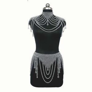 May include: A silver-toned chainmail body harness featuring a high-neck collar, draped shoulder chains, and a waist-cinching belt section. The piece is constructed from interlocking metal rings with multiple hanging chain strands throughout the design.
