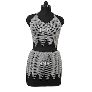 May include: A silver chainmail halter top and matching skirt set featuring interlocking metal rings. The top has a V-neckline and a pointed hem, while the skirt has a matching pointed hem. The text HMFC ARMOR is visible on both pieces.