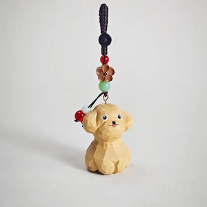 May include: A carved wooden dog figurine with a hanging cord and decorative beads. The dog is light brown with a smiling face and a red tongue. The cord is dark brown with red, green, and white beads.