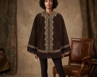May include: A dark brown suede cape featuring intricate gold embroidery along the front opening and neckline. The garment has a structured collar, a silver-toned metal clasp closure, and a fringe hemline that extends around the entire bottom edge.