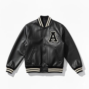 Op de afbeelding: Zwarte varsity jas met een groot wit en zwart letter "A" embleem op de borst. De jas heeft een knoopsluiting, zijzakken en strepen op de kraag, manchetten en zoom. De jas is gemaakt van een leerachtig materiaal.
