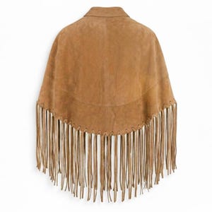 May include: A tan suede poncho featuring a structured collar and a curved hemline. The lower edge is adorned with long, thin suede fringe strips that hang vertically. The garment is constructed with visible whipstitch detailing along the hem.