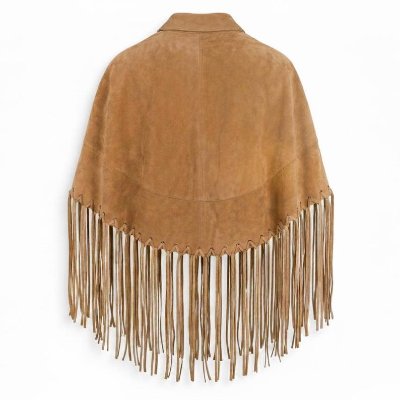 May include: A tan suede poncho featuring a structured collar and a curved hemline. The lower edge is adorned with long, thin suede fringe strips that hang vertically. The garment is constructed with visible whipstitch detailing along the hem.