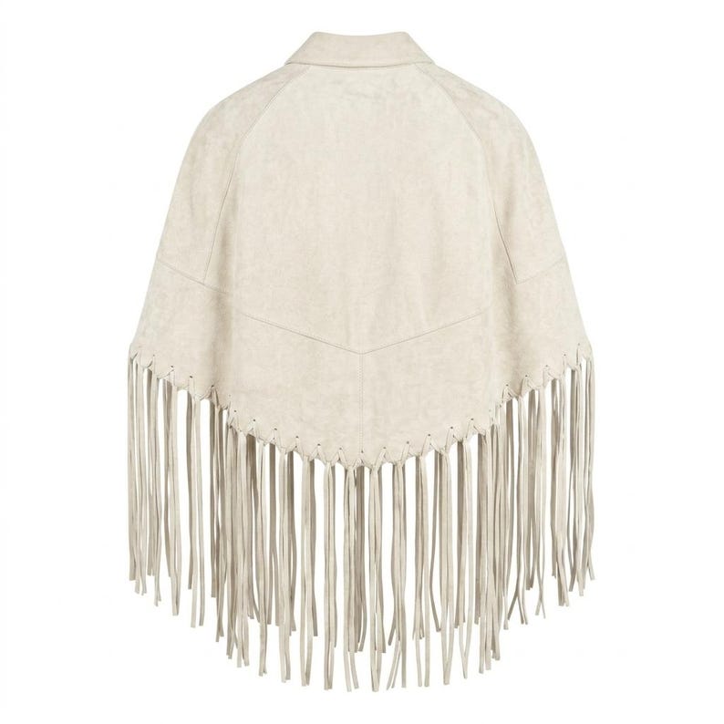 May include: A cream-colored poncho featuring a pointed hemline and long, thin fringe detailing along the bottom edge. The garment has a structured collar and a V-shaped seam across the upper back, showcasing a smooth, suede-like texture throughout.