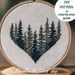 Può includere: Un telaio da ricamo con un motivo a forma di cuore raffigurante una foresta nelle tonalità del verde. Il testo "PDF PATTERN + step-by-step guide" è in un cerchio bianco. Il nome del negozio "PineNeedleStitch shop" è in basso.
