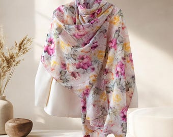 May include: A floral scarf with a light background and a pattern of pink, yellow, and purple roses. The scarf is draped over a white form, showcasing its design. The scarf is made of a lightweight material.