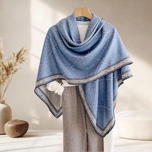 Può includere: Uno scialle blu con un motivo dettagliato e un bordo decorativo è drappeggiato su un appendiabiti. Lo scialle è realizzato in un materiale morbido ed è abbinato a pantaloni grigi e un top bianco. Il design dello scialle include un motivo floreale ripetuto.