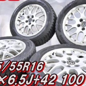 Puede incluir: Cuatro llantas de aleación plateadas de radios múltiples con neumáticos negros, cada una con un logotipo central de Volkswagen. El texto 205/55R16 y 16x6.5J+42 100 5H está impreso en rojo y blanco sobre los neumáticos, indicando las medidas.