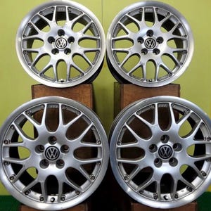 May include: A set of four silver-colored multi-spoke alloy wheels featuring a circular Volkswagen logo at the center of each hub. The wheels have a complex design with numerous thin spokes radiating from the center to the outer rim edge.