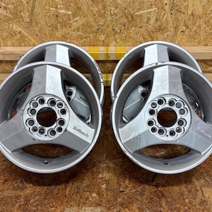 May include: A set of four silver-colored metal alloy wheels, each featuring a three-spoke design and a central hub with multiple bolt holes. The word "Selbach" is embossed on one of the spokes of each wheel. The rims have a metallic finish.