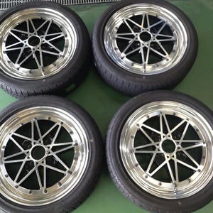 Könnte beinhalten: Ein Satz von vier schwarzen und silbernen Automobilrädern mit Reifen. Jedes Rad verfügt über ein mehrspeichiges Sterndesign mit einer polierten Chrom-Außenfelge und einer zentralen Nabe. Die Reifen bestehen aus schwarzem Gummi mit sichtbarem Profil.