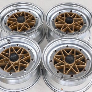 May include: A set of four circular automotive wheels featuring a polished silver outer rim and a gold-colored multi-spoke center design. Each wheel includes a black central hub cap with the word Equip printed in white lettering on the face.