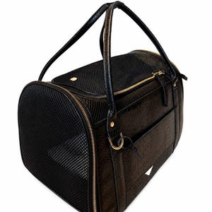 Peut inclure: Un sac de transport pour animaux noir avec un motif texturé en peau de serpent, des panneaux de ventilation en maille noire sur les côtés et le dessus, des fermetures éclair dorées et deux poignées noires. Un petit anneau métallique doré est inclus.