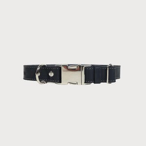 Puede incluir: Un collar para perros azul marino con una hebilla de metal plateado y una anilla en D para sujetar la correa. El collar es de cuero y presenta costuras blancas en los bordes. Dise&ntilde;ado para perros medianos a grandes.