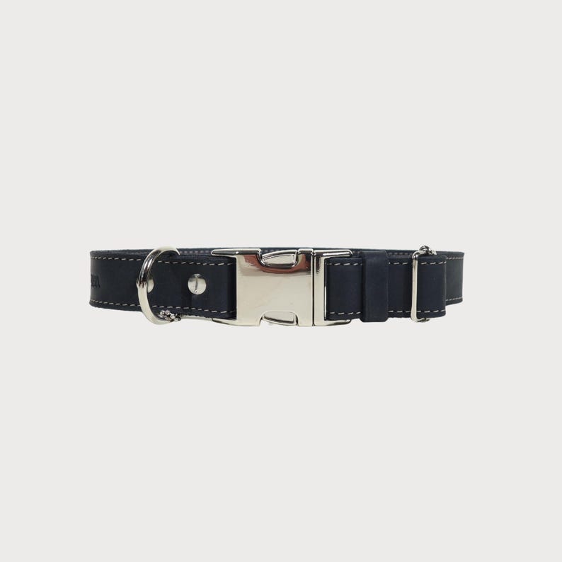 Puede incluir: Un collar para perros azul marino con una hebilla de metal plateado y una anilla en D para sujetar la correa. El collar es de cuero y presenta costuras blancas en los bordes. Dise&ntilde;ado para perros medianos a grandes.