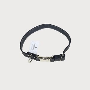Puede incluir: Un collar de perro de cuero negro con costuras blancas. El collar tiene una hebilla de metal plateado y un anillo de metal para sujetar una correa. Una etiqueta blanca con el texto "PAW & REA" est&aacute; adjunta.