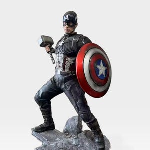 K&ouml;nnte beinhalten: Eine Captain America-Figur, die einen Hammer und einen Schild h&auml;lt. Die Figur befindet sich in einer dynamischen Pose auf einem felsigen Sockel, der sich auf einer schwarzen Plattform mit dem Avengers-Logo befindet. Der Schild ist rot, wei&szlig; und blau mit einem wei&szlig;en Stern. Die Figur tr&auml;gt einen blauen Helm.