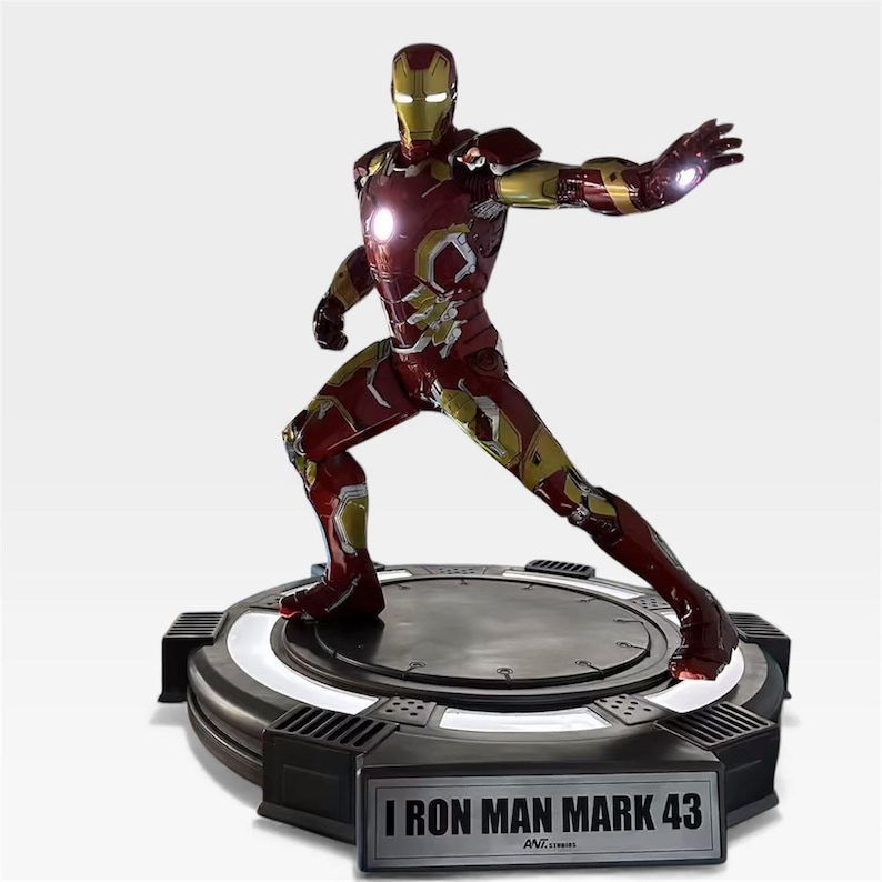 May include: A detailed figurine of Iron Man Mark 43 in a dynamic pose, featuring a red and gold armored suit. The figure stands on a black circular base with a glowing white ring and the text "IRON MAN MARK 43".
