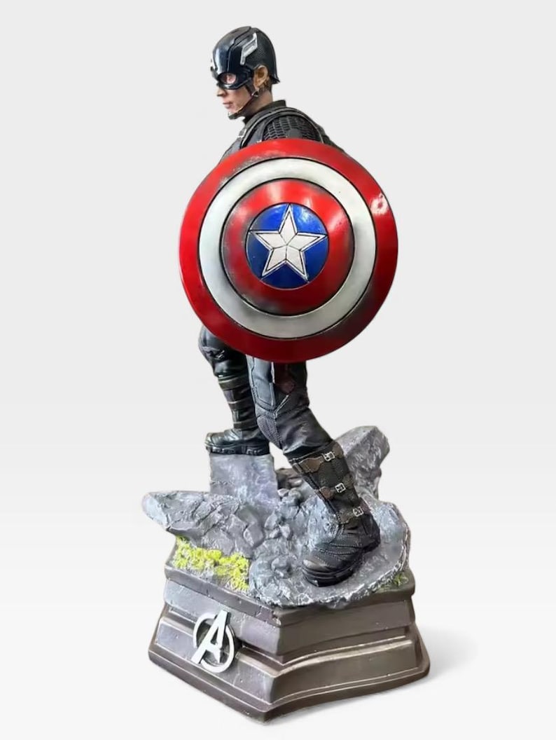 K&ouml;nnte beinhalten: Eine Captain America-Figur, die die Figur in einer dynamischen Pose zeigt, die ihren Schild h&auml;lt. Der Schild hat ein rot-wei&szlig;-blaues Design mit einem wei&szlig;en Stern. Der Sockel der Figur zeigt das Avengers-Logo.
