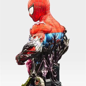 May include: A detailed Spider-Man bust statue, mainly red and blue, in a dynamic pose. The statue has intricate detailing, including a black, textured base with a cityscape and a monster. The design is a blend of comic book and artistic elements.