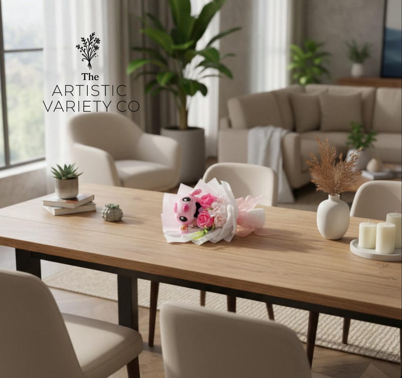 May include: A wooden dining table with a bouquet of pink and white flowers and a stuffed animal. The table also has a small succulent plant, books, and a decorative object. The text "The Artistic Variety Co" is visible.