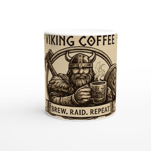 Puede incluir: Taza de café de cerámica blanca con una ilustración de un vikingo. El diseño presenta a un vikingo sosteniendo una taza de café, un hacha y un escudo, con las palabras "VIKING COFFEE" y "BREW. RAID. REPEAT." impresas.