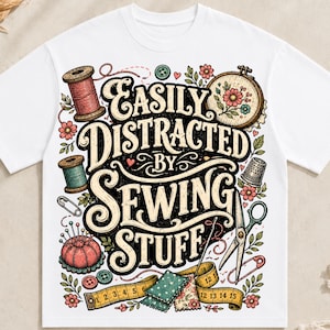May include: A white t-shirt featuring a colorful graphic illustration of sewing supplies including spools of thread, an embroidery hoop, a thimble, scissors, a pincushion, and a measuring tape with the text "Easily Distracted By Sewing Stuff."