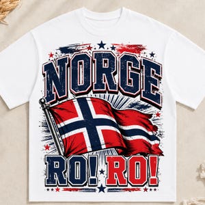 以下が含まれることがあります： 白の半袖Tシャツで、ネイビーと赤の太字で「NORGE RO! RO!」と書かれたグラフィックプリントが特徴です。デザインには、なびくノルウェー国旗、散りばめられた星、赤・白・青の掠れたブラシストロークのアクセントが含まれています。
