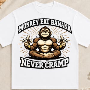 以下が含まれることがあります： 白いTシャツで、蓮華座の姿勢で座り、両手に黄色いバナナを持っている茶色の猿のグラフィックが描かれています。猿の上にはMONKEY EAT BANANAというテキストがアーチ状に配置され、下部のバナーにはNEVER CRAMPというテキストが印刷されています。