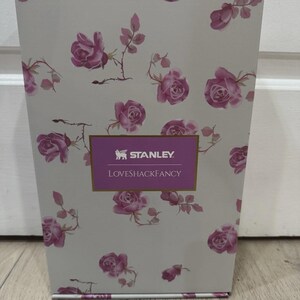 May include: A rectangular box with a floral rose pattern in pink and white. The box has the text "STANLEY LOVESHACKFANCY" in a purple rectangle.