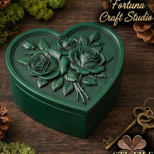 May include: A heart-shaped, dark green box with a detailed relief of roses on the lid. The box is labeled "Design by Fortuna Craft Studio" and "STL FILE". Decorative keys and foliage are in the background.