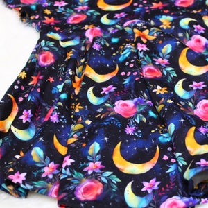May include: Black fabric with a repeating pattern of colorful crescent moons and floral bouquets. The fabric has a watercolor-like effect.