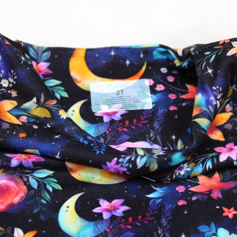 May include: Black fabric with a colorful floral and crescent moon pattern. The fabric has a tag that says "2T".