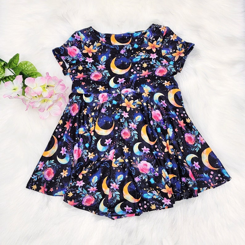 May include: A black dress with a floral and crescent moon print. The dress has short sleeves and a gathered skirt.