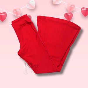 May include: Bright red flared pants. The pants are made of a soft, stretchy material. The pants are folded and displayed on a pink background with a string of paper hearts. The brand name "Pibox" is visible in the lower left corner.