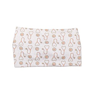 May include: A white headband with a repeating pattern of peach-colored stethoscopes and medical crosses. The headband is a soft, stretchy fabric, suitable for various head sizes. The design is simple and clean, perfect for medical professionals or anyone who appreciates medical-themed accessories.