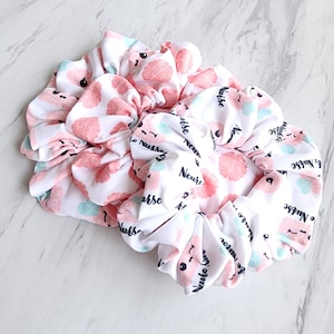 May include: Two white scrunchies with a pink brain and the text "Neuro Nurse" printed on them.