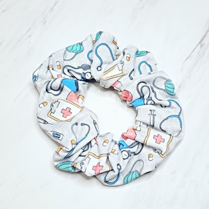 May include: Gray scrunchie with a white background and a pattern of medical symbols, including stethoscopes, syringes, pills, and bandages.