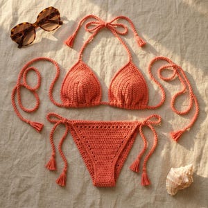May include: A bright orange crochet bikini set featuring a triangle top with halter neck ties and matching side-tie bikini bottoms. The set is accompanied by a pair of brown tortoiseshell sunglasses and a single white seashell.
