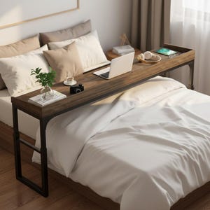 May include: A dark brown, rectangular bed desk with black metal legs. The desk is positioned over a bed with white bedding and pillows. A laptop, coffee cup, camera, and plant are on the desk. The desk is designed for working or eating in bed.