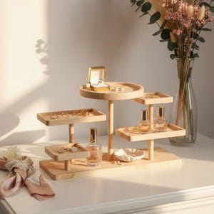 Könnte beinhalten: Ein mehrstöckiger Schmuck-Organizer aus Holz mit verschiedenen Ablagen und Plattformen. Der Organizer enthält Ringe, Ohrringe und Parfümflaschen. Eine kleine Ringschatulle ist auf der obersten Ebene geöffnet.