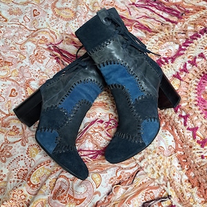 Könnte beinhalten: Ein Paar Wildleder-Patchwork-Stiefel in Marine- und Blautönen. Die Stiefel haben ein Schnürdesign und einen klobigen schwarzen Absatz. Die Stiefel liegen auf einem gemusterten Stoff mit Fransen.