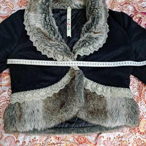 K&ouml;nnte beinhalten: Schwarze Bolerojacke mit Kunstfellbesatz und Spitzenkragen. Die Jacke hat einen Knopfverschluss und ein Etikett mit dem Text "my♡se". Die Jacke ist ca. 71 cm lang.